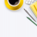 A yellow note pad and keyboard, surrounded by pencils on a white desk